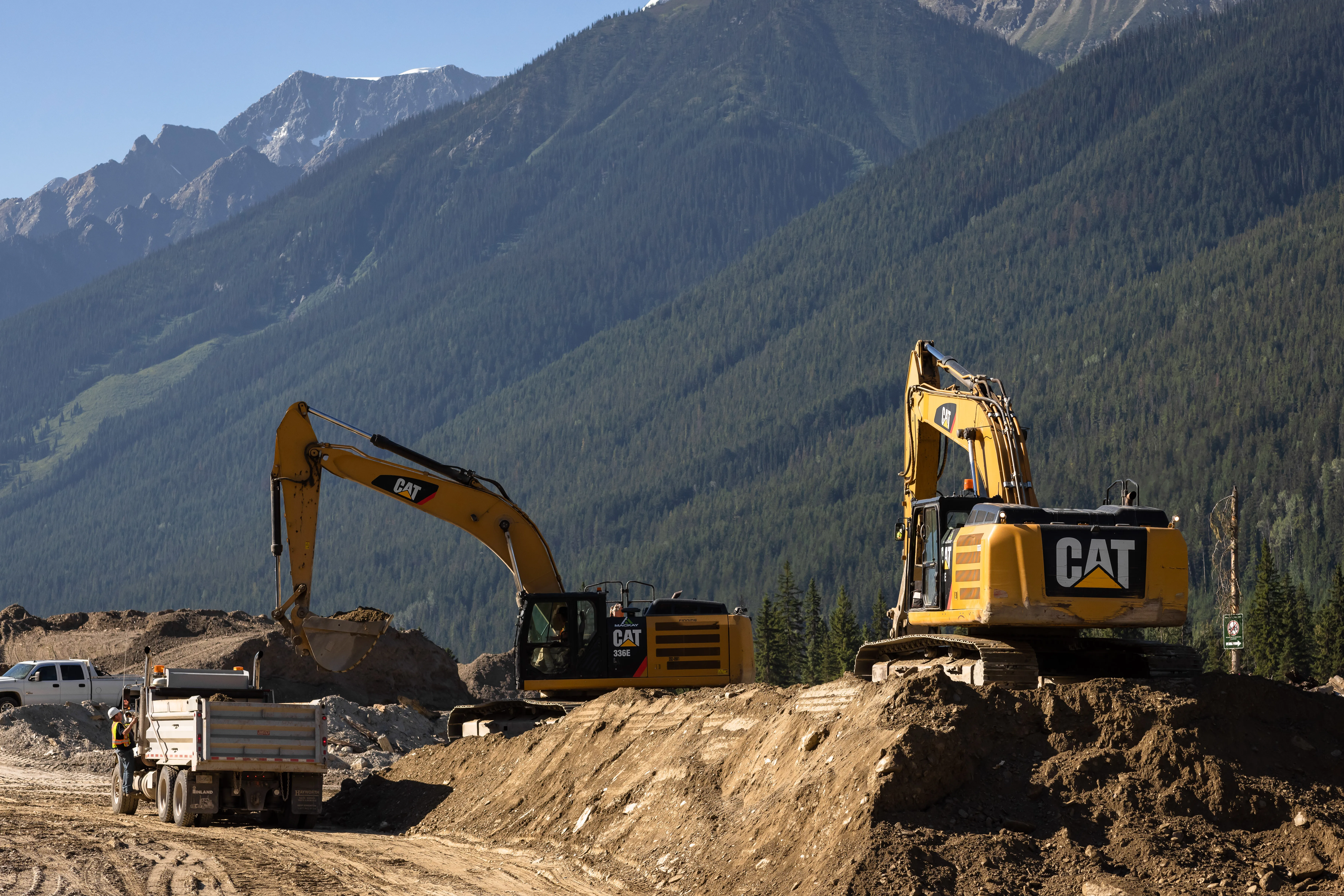 Two Mackay excavators load a rock truck beneath a forested mountainside at first light
