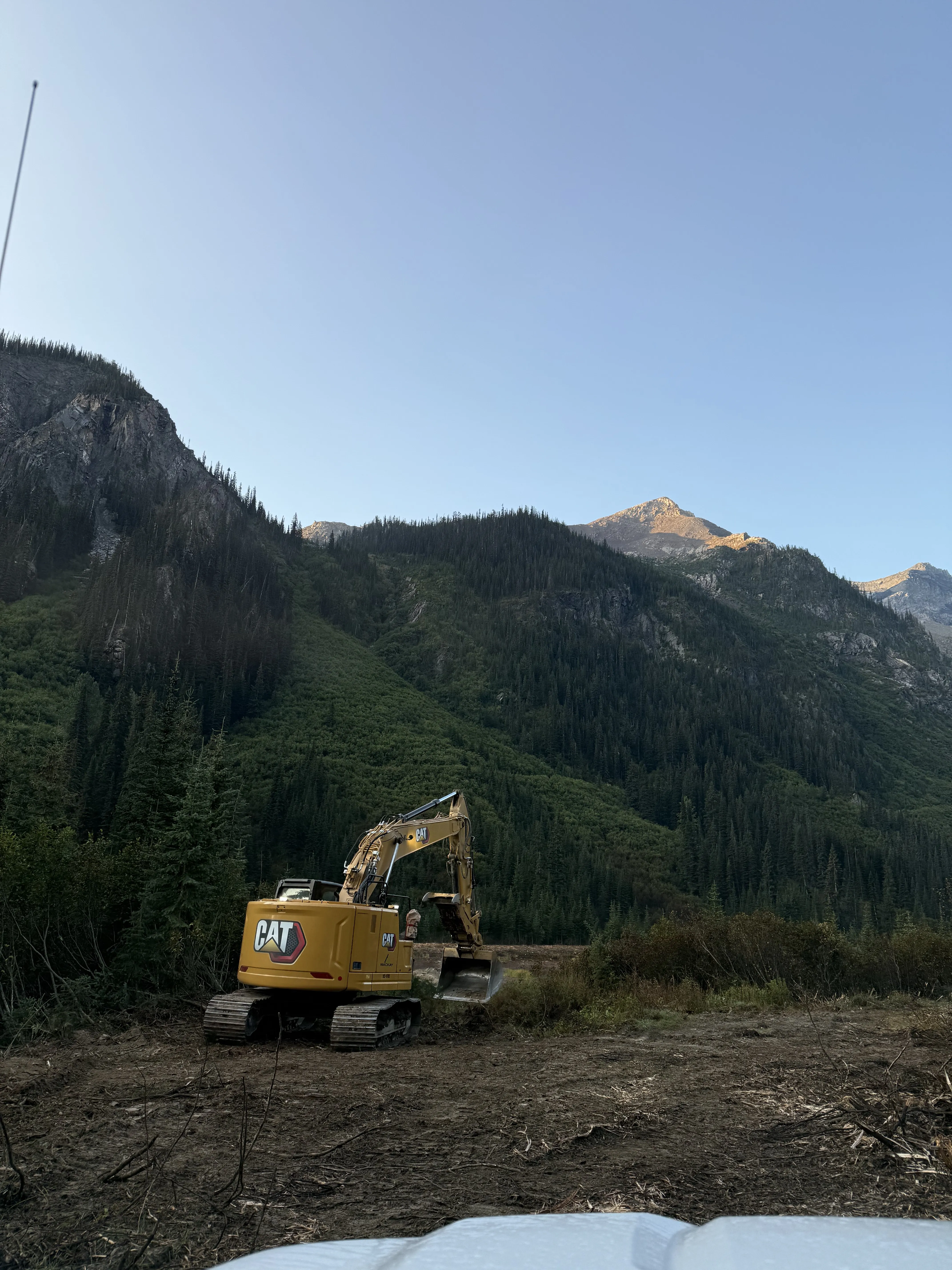 Excavator working a creek restoration site beneath a forested mountainside