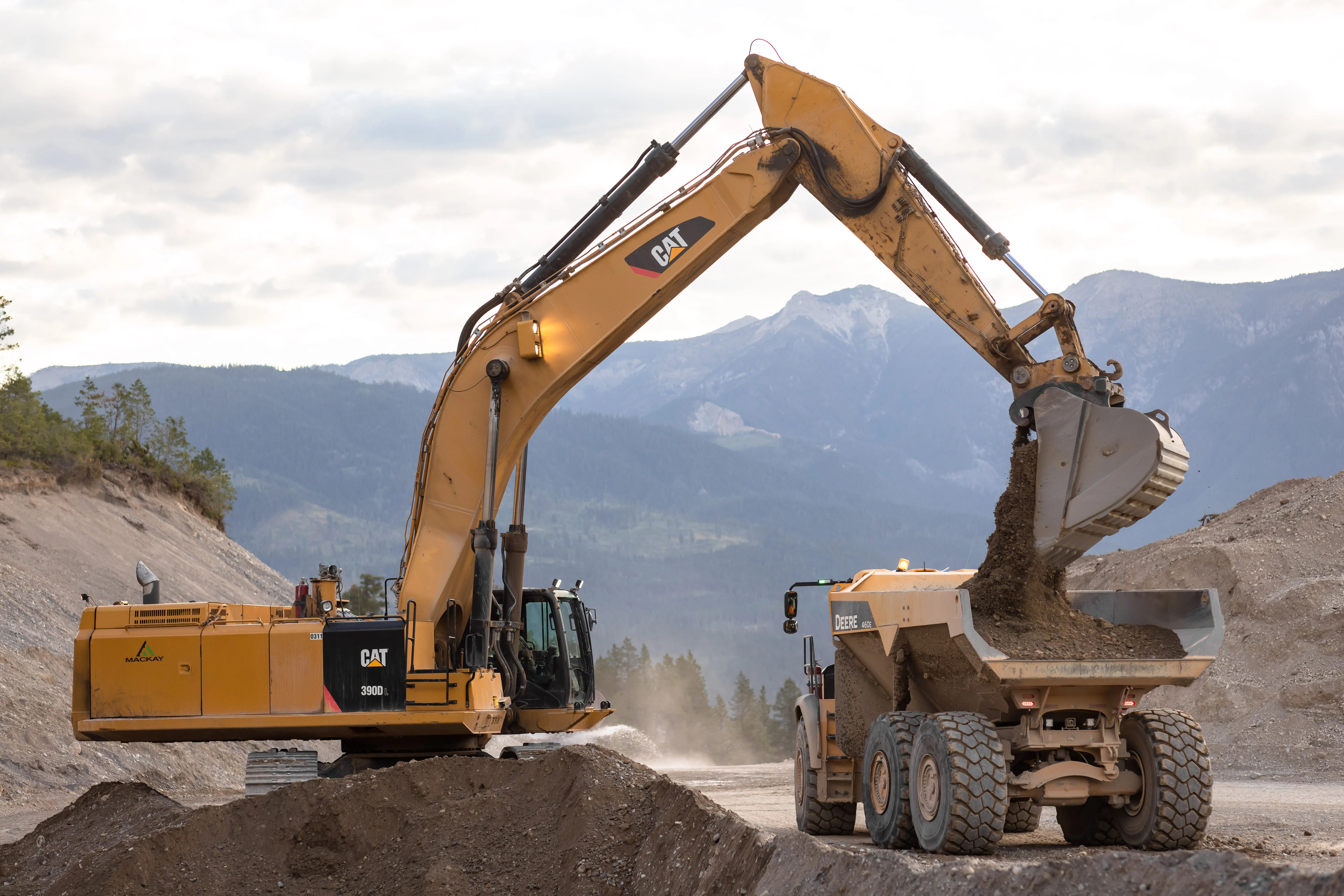 Mackay excavator loading an articulated rock truck against a mountain backdrop